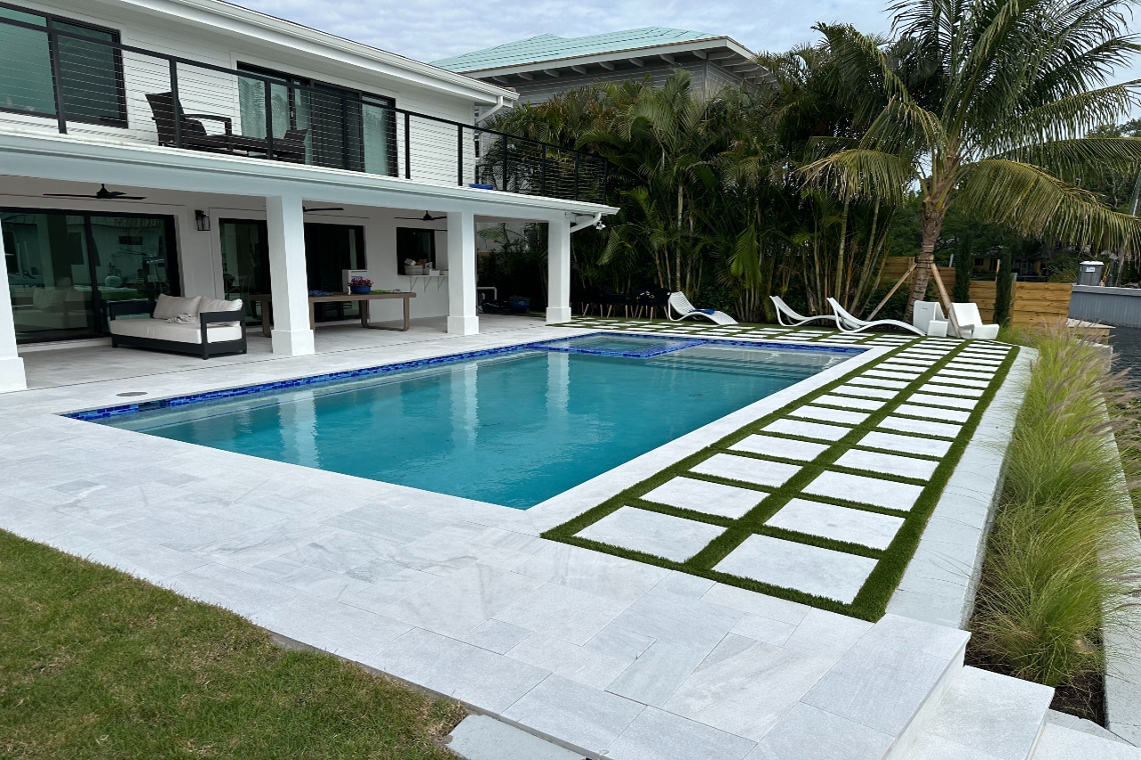 Traditional rectangular pool surrounded by white paver patio and stepping stones.